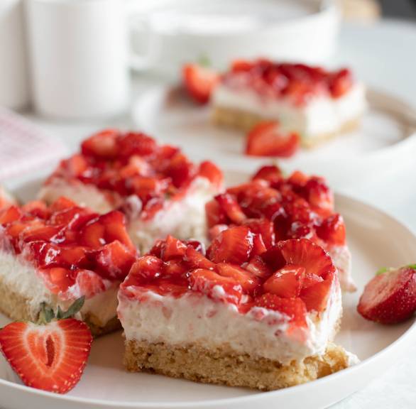 Mehrere Stücke selbstgebackener Blechkuchen mit Erdbeeren und Pudding-Quark-Creme auf einem Kaffeetisch