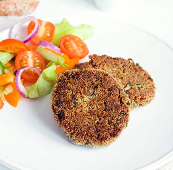 zwei selbstgemachte, gebratene Linsenfrikadellen angerichtet neben gemischtem Salat auf einem Teller