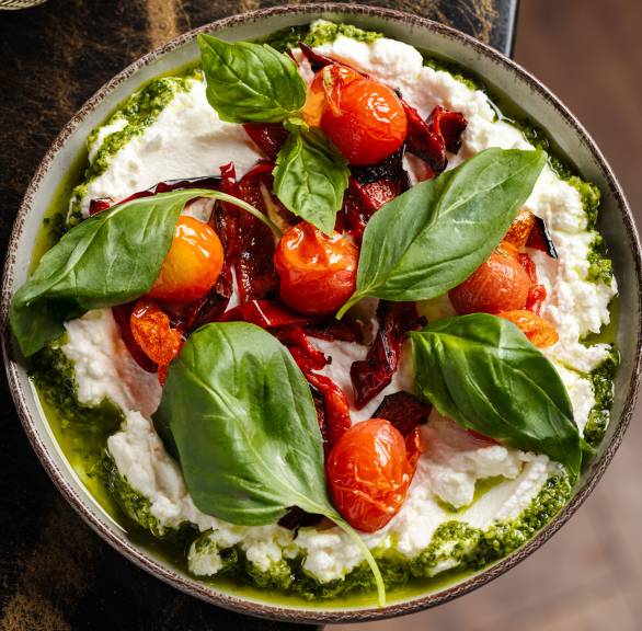 Whipped Burrata Dip mit gerösteten Kirschtomaten und gegrillter Paprika garniert mit frischem Basilikum auf einem Tisch