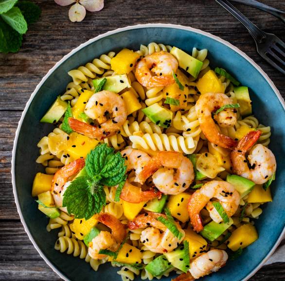 Nudelpfanne aus Fusilli mit Garnelen, Mango, Avocado getoppt von frischer Minze auf einem Tisch
