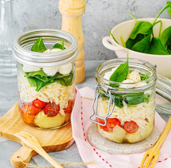 Italienischer Schichtsalat in zwei Weckgläsern mit Risoni, Tomaten, Mozzarella, Artischocken und Dressing
