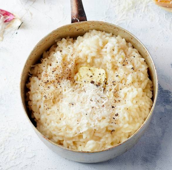 Selbst gekochtes Risotto in einem Stieltopf auf einem Tisch, daneben verschiedene Zutaten