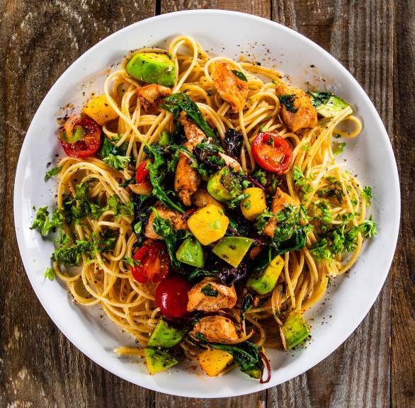 Spaghetti "Tropicana" mit gebratenen Hähnchenbrustfiletstücken und Würfeln von Avocado und Mango angerichtet auf einem Pastateller mit frischen Kräutern