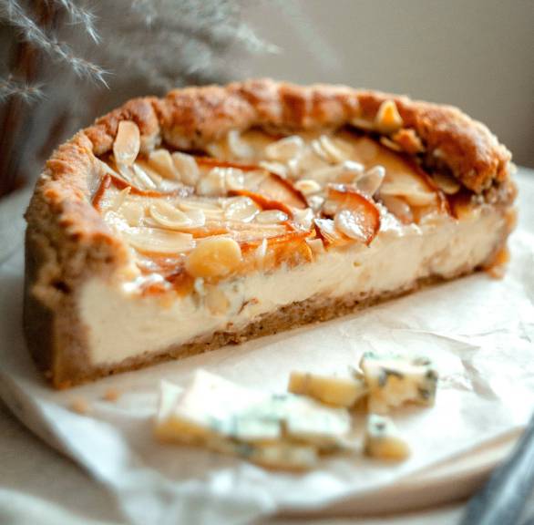Ein halber Gorgonzola-Cheesecake mit Birnen und Mandeln angerichtet auf einer Kuchenplatte