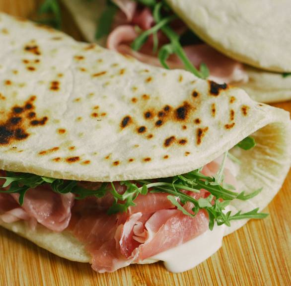 Zwei selbstgebackene Piadinas gefüllt mit Schinken, Käse und Rucola auf einem Holzbrett