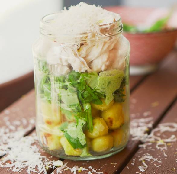 Ein Weckglas als Street Cup mit Schichten aus Gnocchi,  Salsa Verde, Rucola und Hähnchen auf einem Holztisch