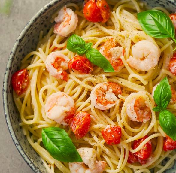 Eine Schale mit One Pot mit Spaghetti, Garnelen, Kirschtomaten und Zitronen-Ricotta garniert mit Basilikumblättern auf einem Tisch