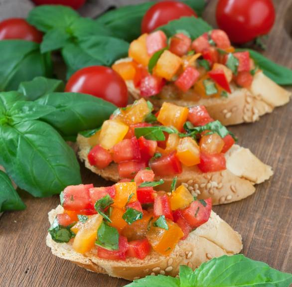 Bruschetta mit gelben und roten Datterini, Basilikum und Olivenöl angerichtet von Serena Loddo auf einem Holzbrett