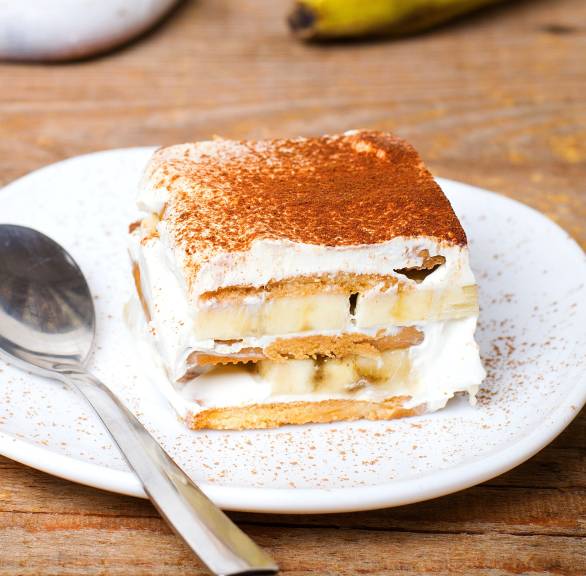 Ein Stück Schoko-Bananen-Tiramisu auf einem Dessertteller, daneben frische Bananende