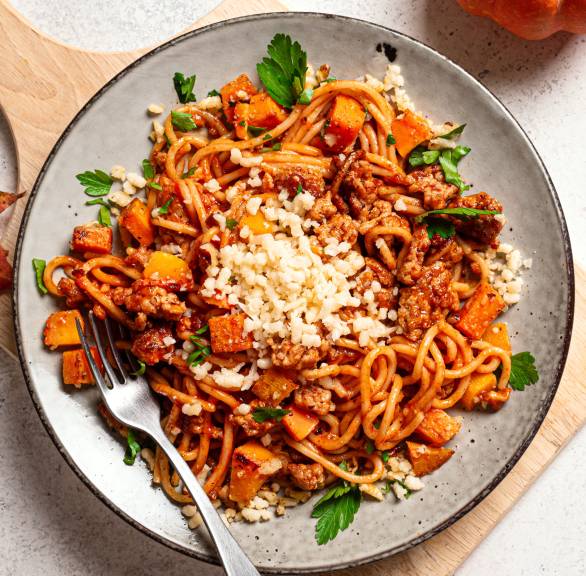 Spaghetti mit Kürbis-Hackfleisch-Bolognese angerichtet auf einem Pastateller getoppt von geriebenem Parmesan auf einem Esstisch