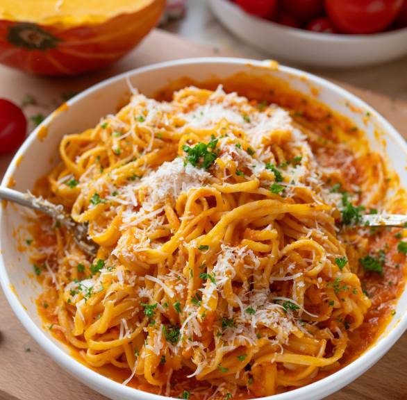 Spaghetti mit Kürbis-Sugo angerichtet auf einem pastateller getoppt von frisch geriebenem Parmigiano Reggiano