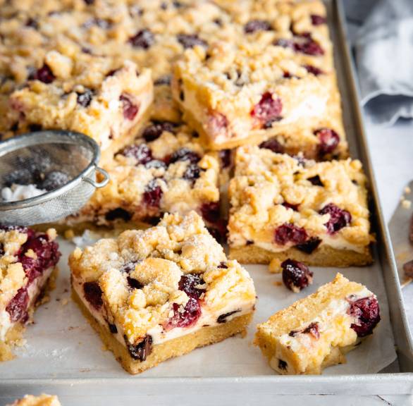 Stracciatella-Käsekuchen mit Kirschen und Streuseln in Stücke geschnitten auf einem Backblech