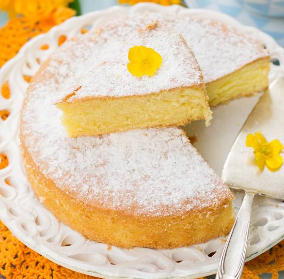 Torta Margherita angeschnitten auf einer Kuchenplatte garniert mit Blütern