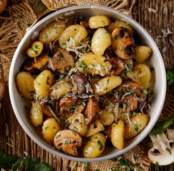 Pfanne mit gebratenen Champignons und Gnocchi in Knoblauchbutter getoppt von Parmesan auf eine Holztisch