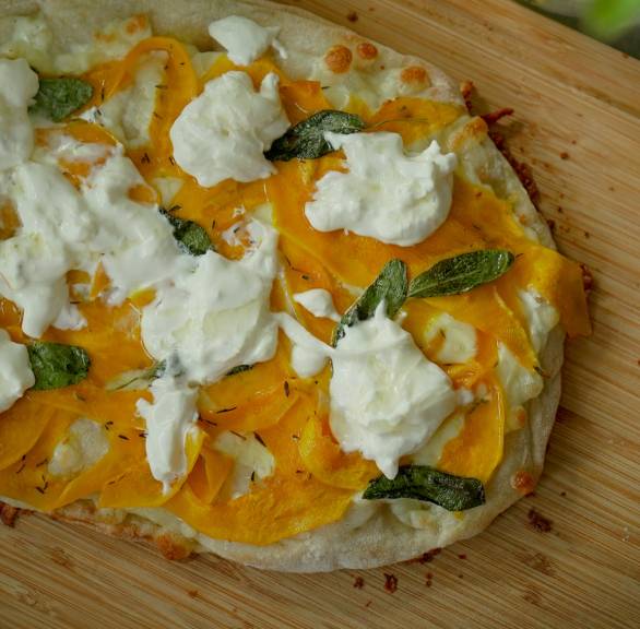 Gebackene ganze Pinsa belegt mit dünnen Kürbissalten und zerrupftem Burrata