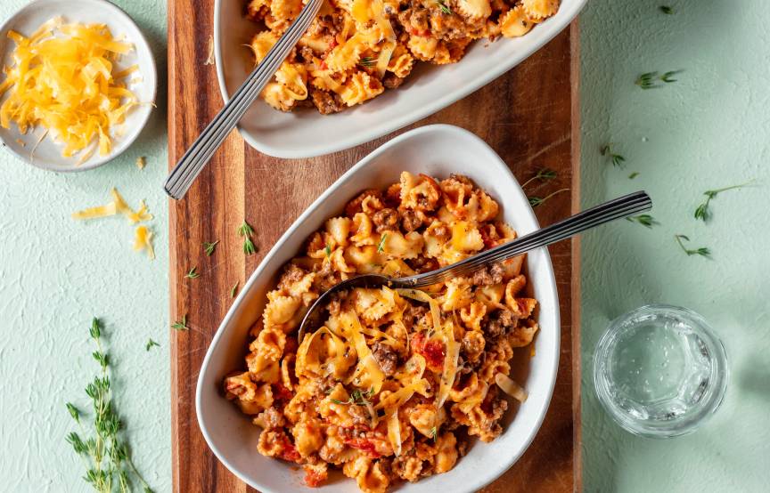One Pot Pasta mit Bolognese in zwei tiefen Tellern, daneben Käseraspel in einer Schüssel