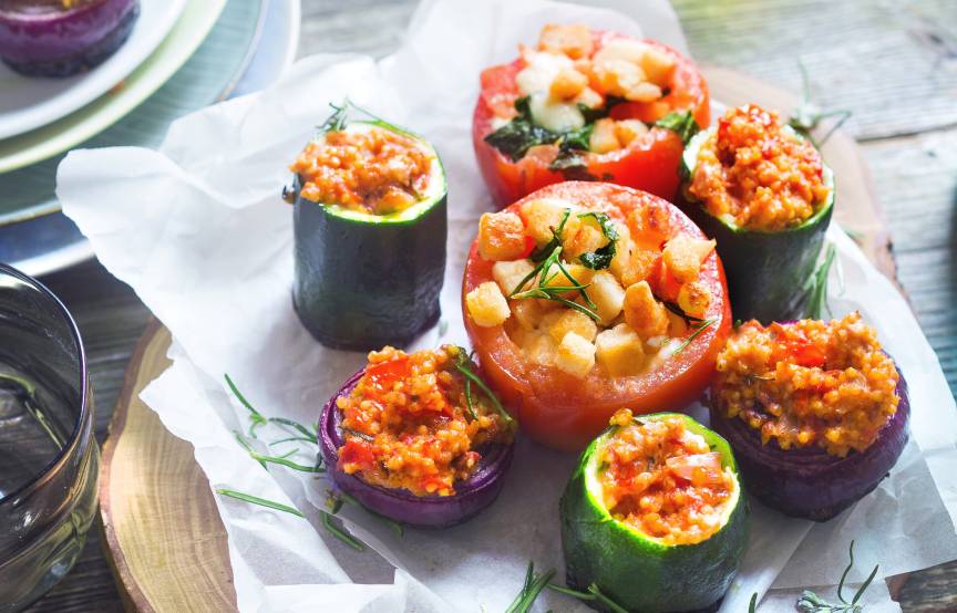 Verschiedene Gemüsestücke gefüllt mit Hirsemischung gegrillt auf einem Holzbrett, daneben Olivenöl in einer Flasche