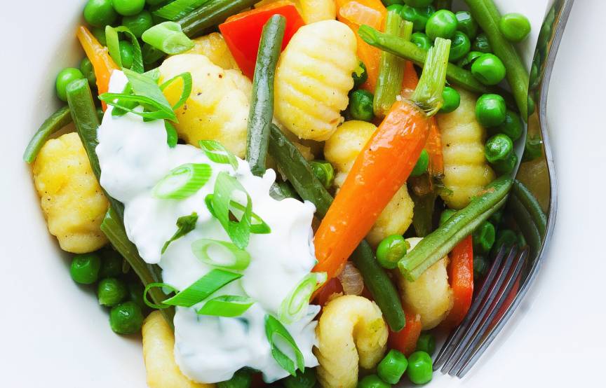 Gnocchi-Gemüse-Pfanne auf einem Teller getoppt mit Joghurt-Dip