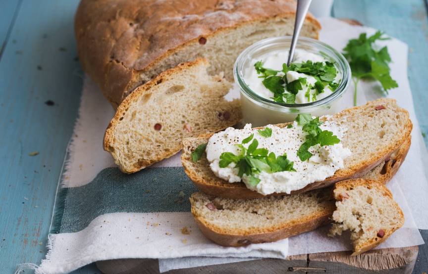Kartoffelbrot angeschnitten auf einem Tisch, daneben einige Scheiben mit Joghurt-Dip und frischen Kräutern
