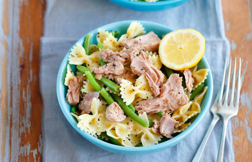 Pastasalat in einer Schüssel auf einem Tisch mit Thunfisch, grünen Bohnen und garniert mit einer halbe Zitrone