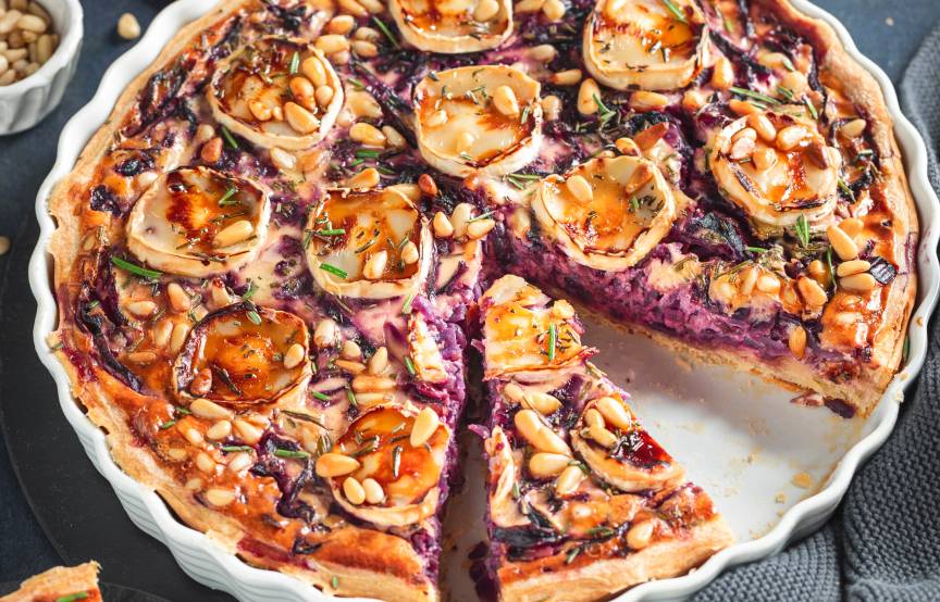 Rotkohlquiche mit Ziegenkäsetalern getoppt angeschnitten in einer Tarteform, daneben Honig