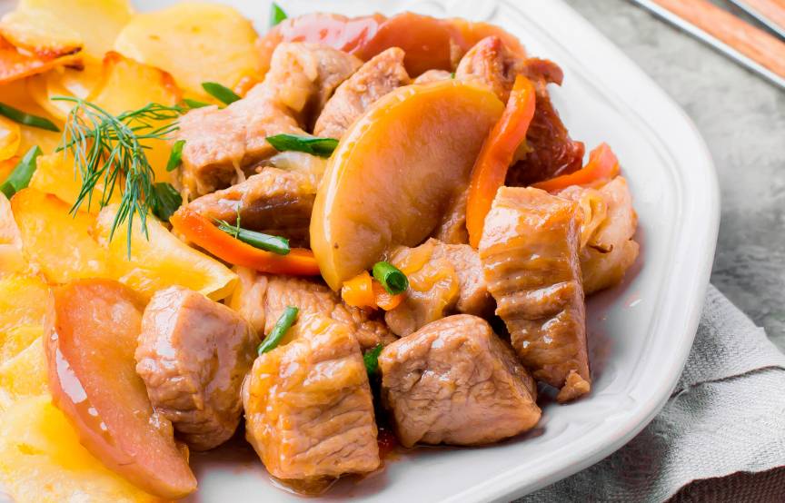 Schweinegulasch auf einem Teller mit Äpfeln und Kartoffelgratin