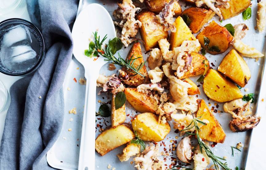 Tintenfisch und Kartoffeln aus dem Ofen auf einem Backblech, daneben ein Teller und eine Wasserflasche