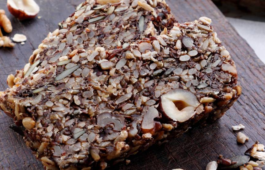 Vollkornbrot in Scheiben auf einem Holzbrett, daneben Nüsse