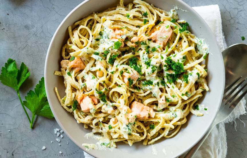 Vollkornnudeln mit Lachs und cremiger Sauce getoppt von frischen Kräutern in einem tiefen Teller