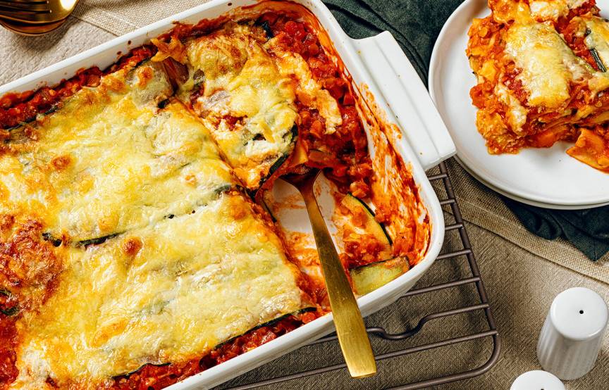 Vegetarische Zucchinilasagne in einer Auflaufform, ein Stück auf einem Teller daneben