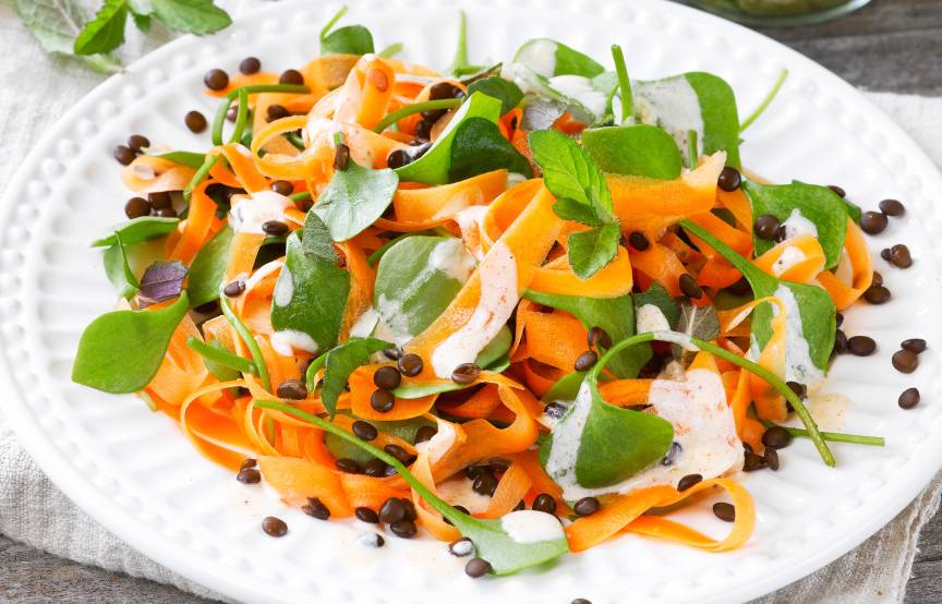 Möhren-Rohkost-Salat auf einem Teller getoppt mit Linsen und Schmand-Dressing