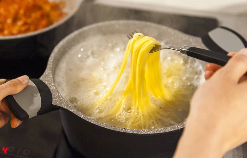Frau schaut nach Spaghetti, die in Salzwasser kochen