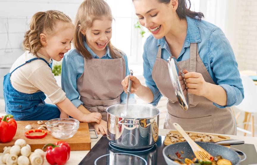 Mutter in der Küche mit zwei Kindern beim Kochen eines Gemüsegerichts und Pasta