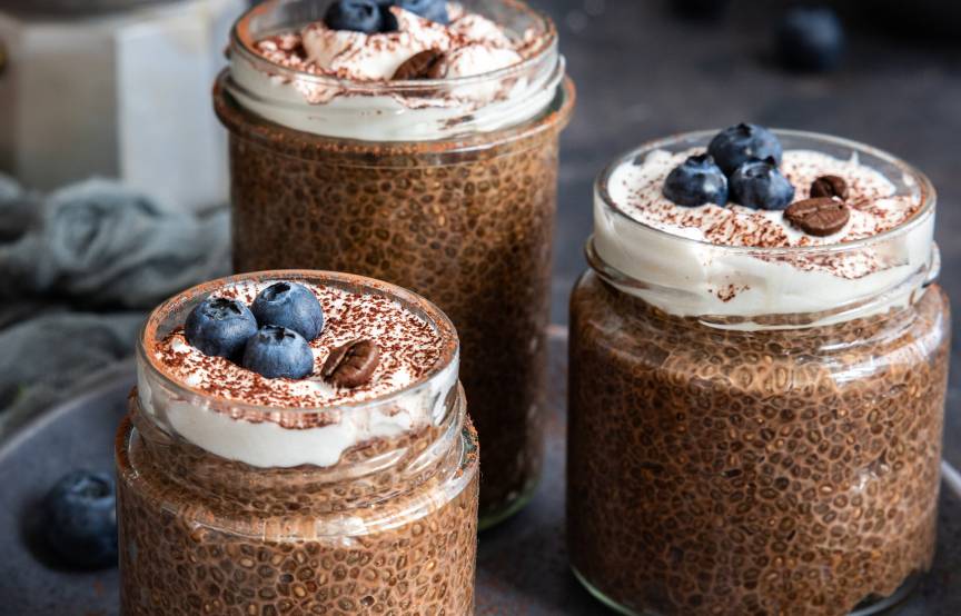 Veganer Chiapudding mit Espresso in drei Weckgläsern auf einem Tablett dekoriert mir Blaubeeren und Espressobohnen