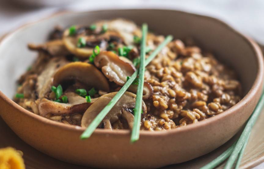 Veganes Hafer-Risotto mit Pilzen in einer Tonschale garniert mit frischen Kräutern