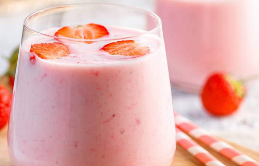 Erdbeer-Smoothie in zwei Gläser gefüllt und mit frischen Erdbeerstücken garniert auf einem Holzbrett