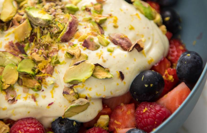 Obstsalat aus Beeren mit Leinöl-Quark-Creme in einer grauen Schale getoppt mit Zitronenabrieb und Pistazien