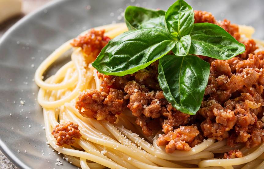 Spaghetti mit Bolognese-Soße auf einem runder Teller getoppt von frischem Basilikum