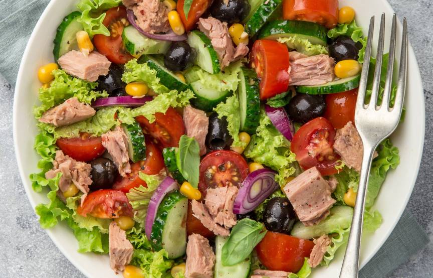 Thunfischsalat mit Mais, Oliven, Gurke, Zwiebel und Tomate auf einem Teller garniert mit frischer Petersilie