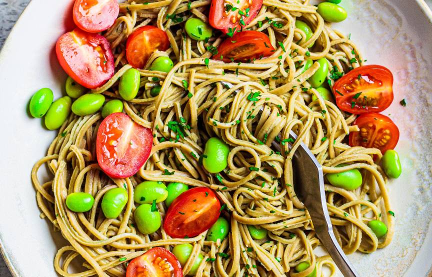 Edamame-Spaghetti auf einem Teller getoppt mit Kirschtomaten und Edamame-Bohnen sowie frischer Petersilie
