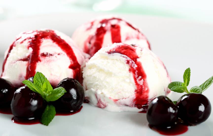 Drei Kugeln Amarena-Eis auf einem Dessertteller garniert mit Amarena-Kirschen und Minze