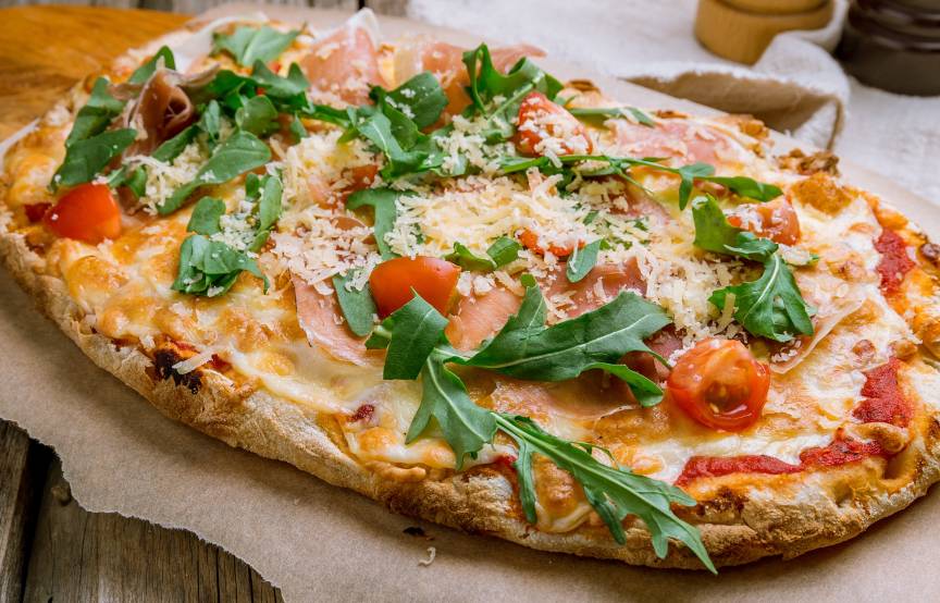 Ovale Pinsa mit knusprigem Boden und buntem Belag auf einem Holzbrett 