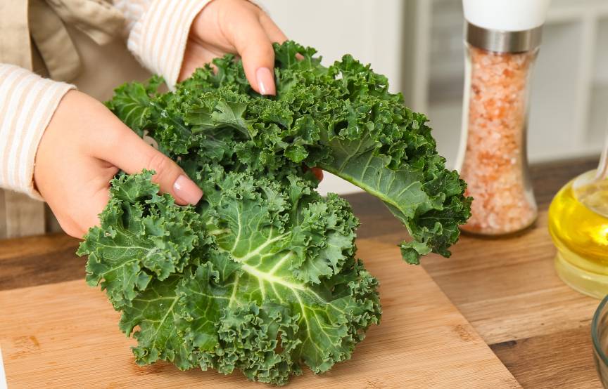 Eine Frau zerreißt Grünkohlblätter über einem Holzbrett in einer Küche