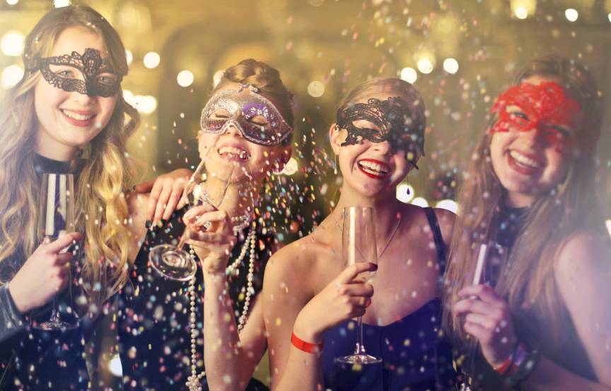 Vier Frauen feiern maskiert Silvester in Venedig und halten Proseccogläser in der Hand