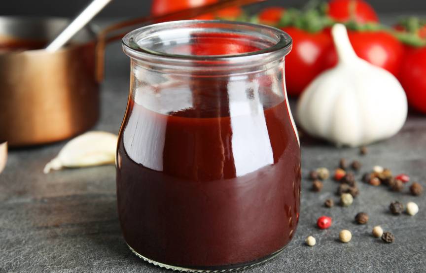 Selbstgemachte dunkle Soße in einem Einmachglas, dahinter verschiedene Zutaten und ein kupfernen Topf