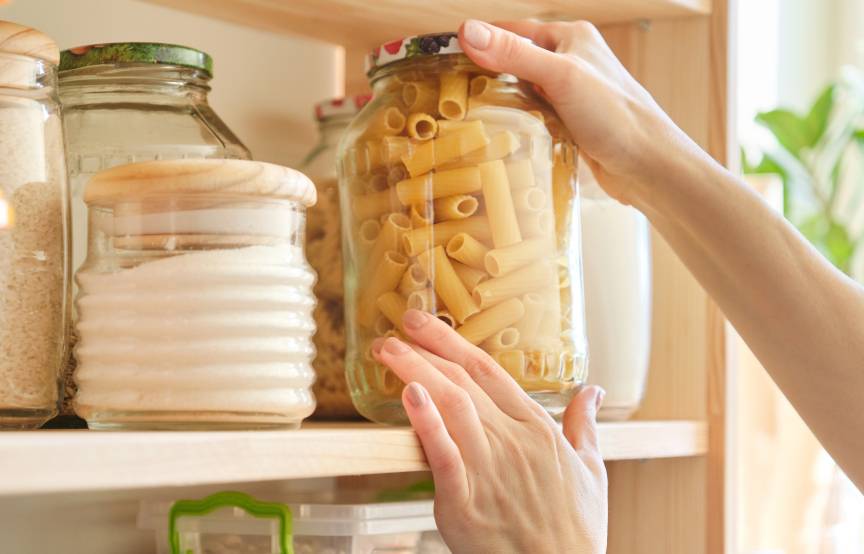 Eine Frau nimmt gerade ein Glas Nudeln aus einem Vorratsschrank