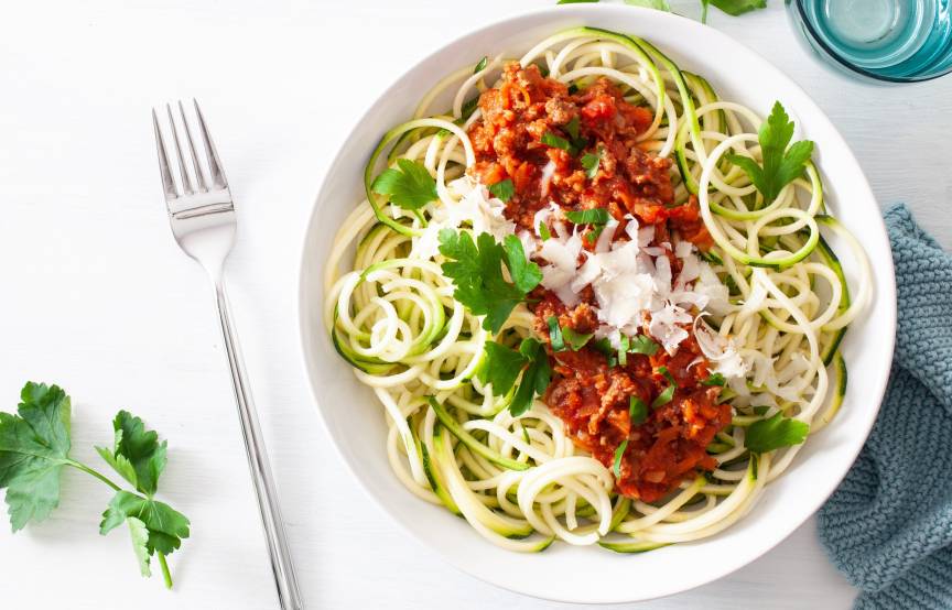 Zucchini-Nudeln mit Bolognese und Parmesan angerichtet auf einem Teller