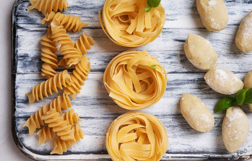 Selbstgemachte Pasta, Fusilli und Bandnudeln auf einem Tablett neben frischen Gnocchi