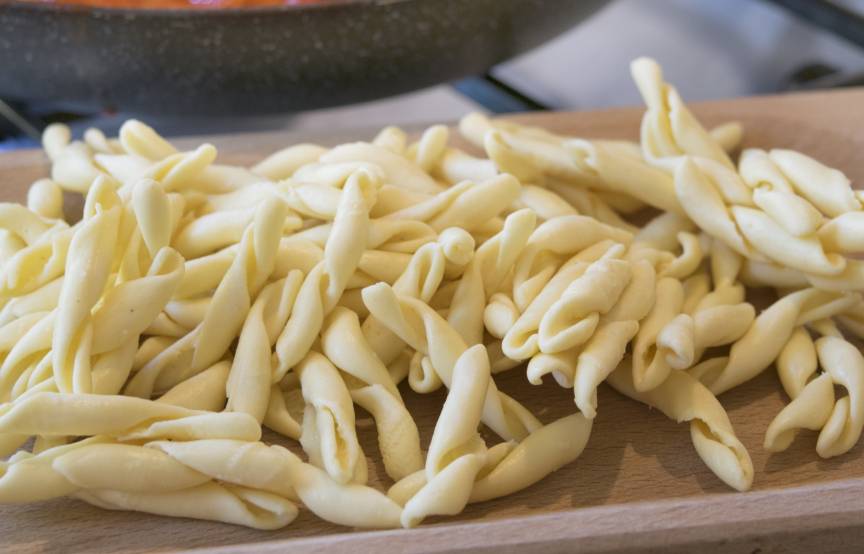 Selbstgemachte frische Nudeln auf einem Holzbrett, dahinter Tomatensoße in einer Pfanne