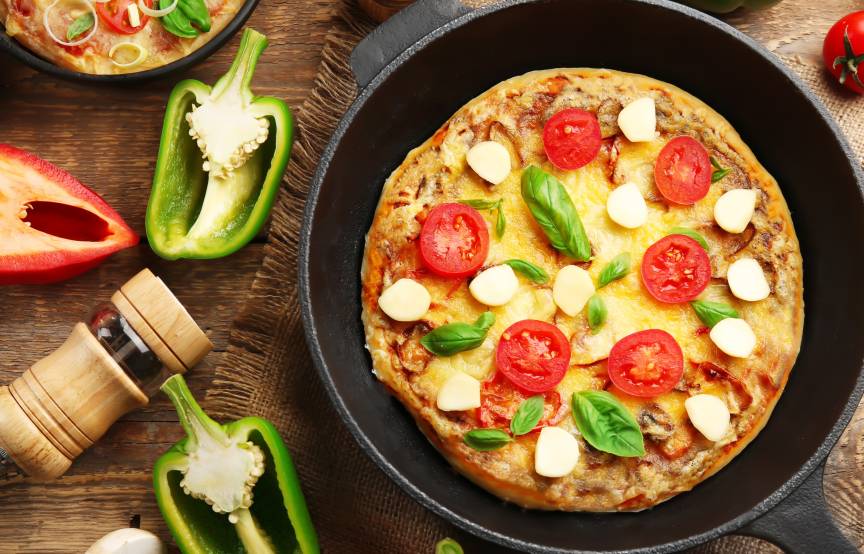 Gebackene Pfannenpizza auf einem Holztisch umgeben von frischen Zutaten